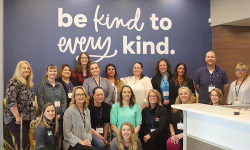 A diverse group of women smiling in front of a sign.